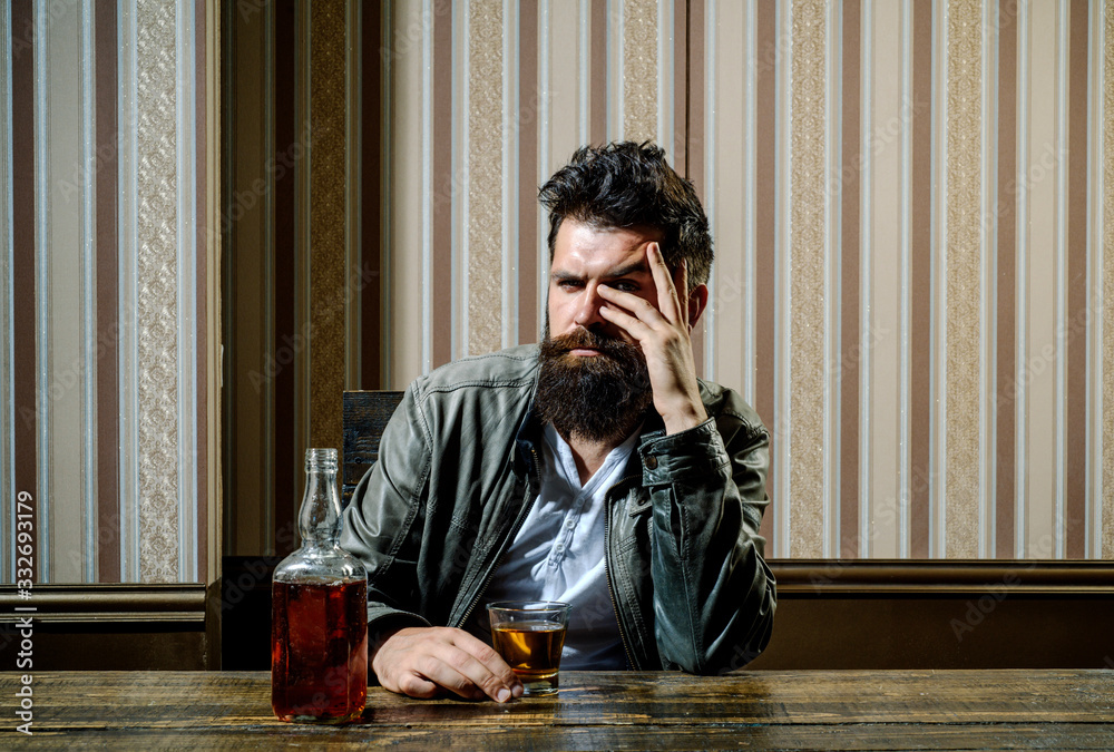 Fototapeta premium Bearded brutal hipster man drinking expensive cognac. Serious problems with alcohol addiction. Alcoholism treatment. Handsome man drinking alone.