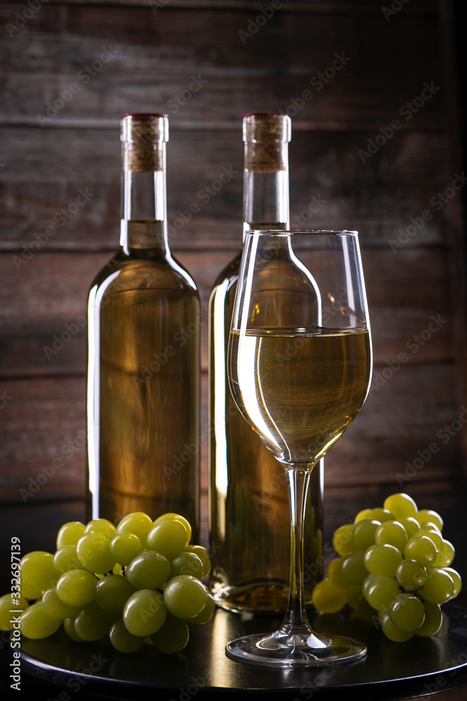 Obraz premium Two white wine bottles with a glass and grapes on a wooden background