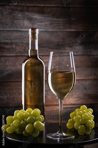 Wite wine bottle and a full glass and grapes on a table on a wooden background