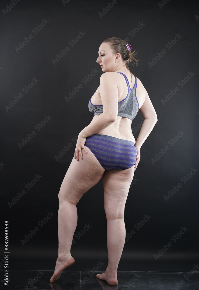 Obraz premium plus size woman shows her body in stretch marks and hair with cellulite and encourages you to love and accept yourself in any way . black background in the Studio. full- length photo.
