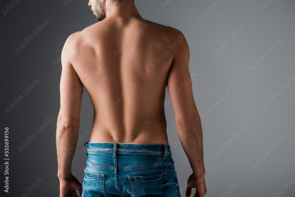 Naklejka premium Back view of sexy shirtless man in jeans on grey