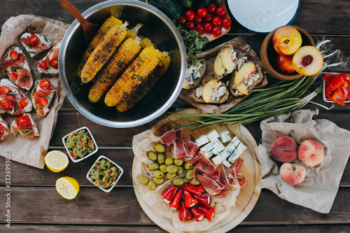 Summer picnic or BBQ food concept. Selection of vegetables, sandwiches, grilled corn and meat. Top view table scene on a wood background.