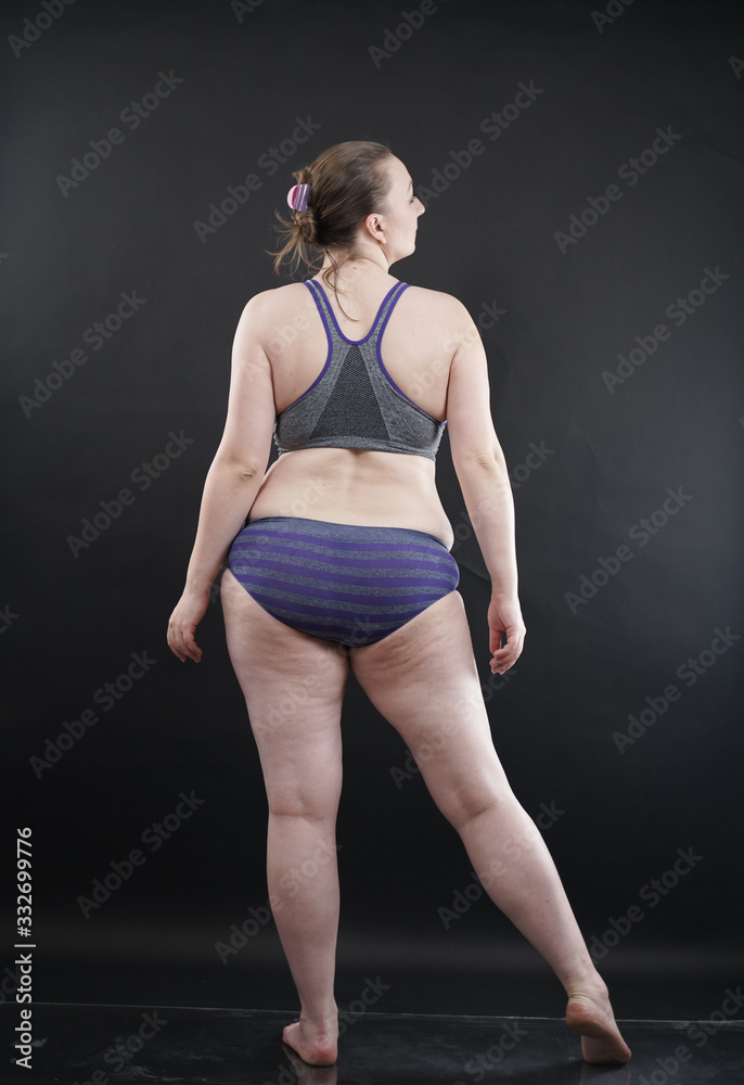 Obraz premium plus size woman shows her body in stretch marks and hair with cellulite and encourages you to love and accept yourself in any way . black background in the Studio. full- length photo.