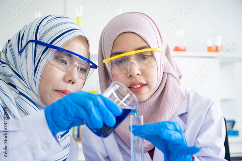 Two Asian bio chemists making the experiment in laboratory together. Expert chemistry scientists inspecting and testing a vaccine sampling on testing plate. Muslim pharmaceutical scientists in lab.
