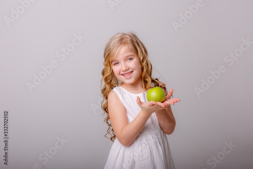 a little girl with a green Apple in her hands smiles sweetly on a gray background