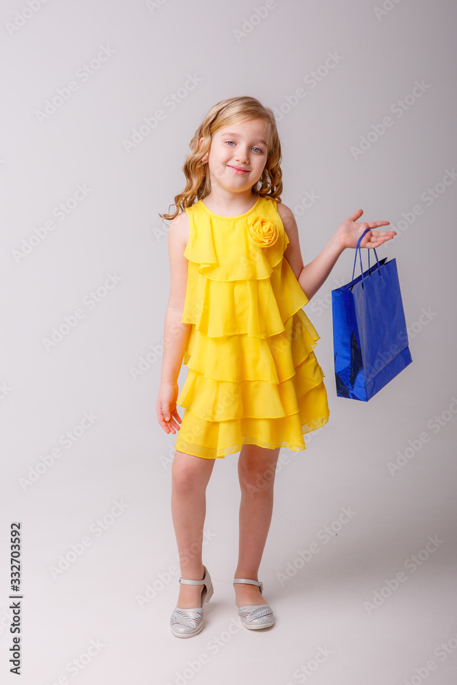 a little girl in a yellow dress with a shopping bag dancing on a gray background a little girl in a yellow dress with a shopping bag dancing on a gray background