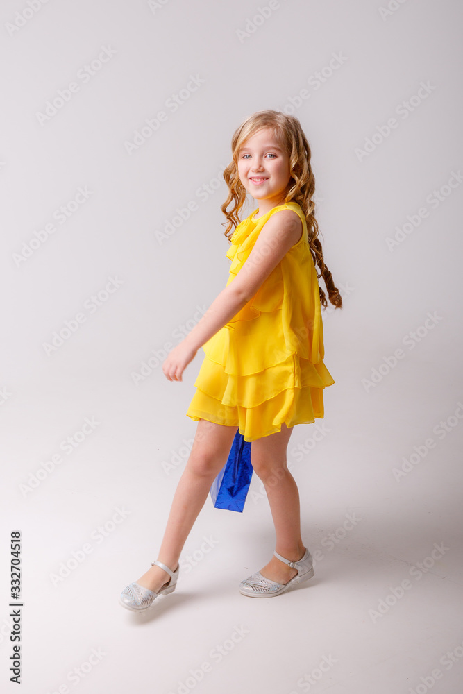 a little girl in a yellow dress with a shopping bag dancing on a gray background a little girl in a yellow dress with a shopping bag dancing on a gray background