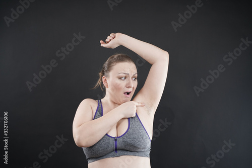 unhappy woman shows her unshaved armpit. plus size middle age woman is not happy with hair in her armpits. Caucasian girl is emotional sad and upset. black background in the photo Studio. © goldeneden