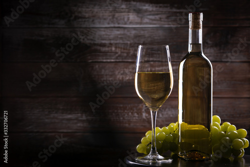 White full wine bottle and wineglass with grapes on a table on a wooden background