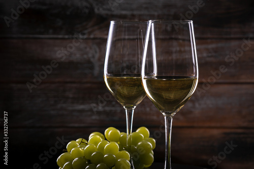Two full white wine glasses with grapes on a table on a wooden background
