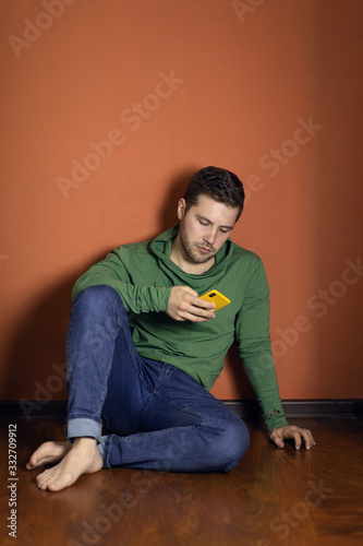 Portrait of a young man of attractive appearance with a beard, mustache and fashionable hairstyle, dressed in a casual green longsleeve and jeans, posing in the Studio on an orange background.