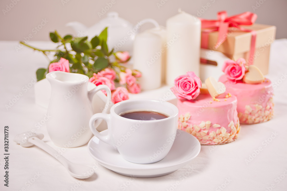 A cup of tea, pink roses and small cakes on the white table