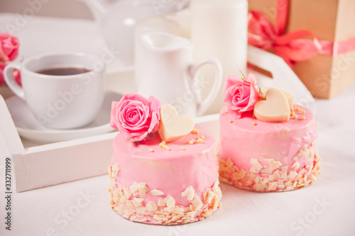 A cup of tea, pink roses, gift box and small cakes on the white table. Romantic concept.