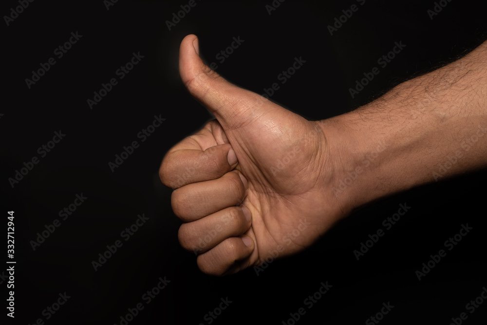 Male strong hand showing thumb up gesture. Closeup front view photograph on a black studio background. 