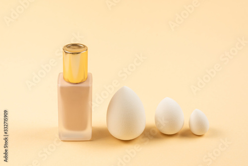 Small, medium and large  white beauty blender and makeup foundation on beige background.