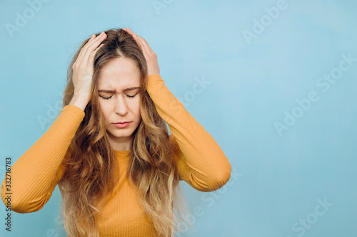 portrait of a close-up of a girl on a blue background. The woman is holding on to her head. Headache. Epidemic covid-2019. Virus 2020. people with flu syndromes. Seasonal cold.