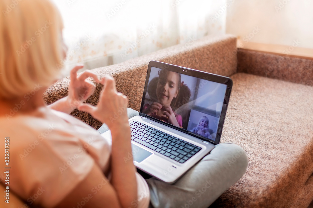 Cute girl talking with her grandmother within video chat on laptop, life in quarantine time - obrazy, fototapety, plakaty 