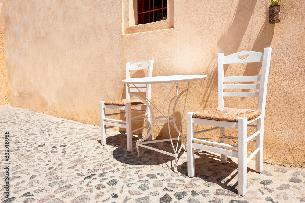 Two white wooden chairs with table on the street. Traditional greek architecture on Santorini island, Greece.