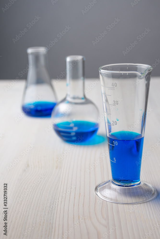 Top view of three different glass test tubes with blue liquid and selective focus, on white wooden table and gray background, vertical Top view of three different glass test tubes with blue liquid and selective focus, on white wooden table and gray background, vertical