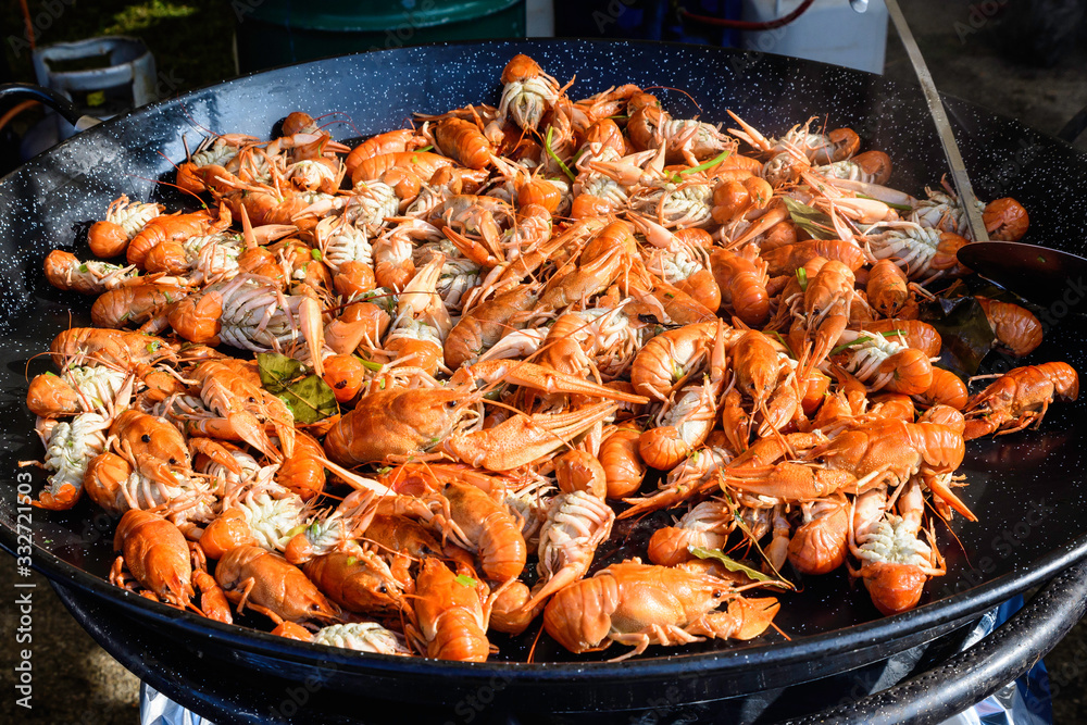 Close up of large portion of cooked shrimps with tomato sauce and yellow lemons in a large pan at a street food festival, ready to eat healthy seafood, beautiful orange monochrome outdoor background Close up of large portion of cooked shrimps with tomato sauce and yellow lemons in a large pan at a street food festival, ready to eat healthy seafood, beautiful orange monochrome outdoor background