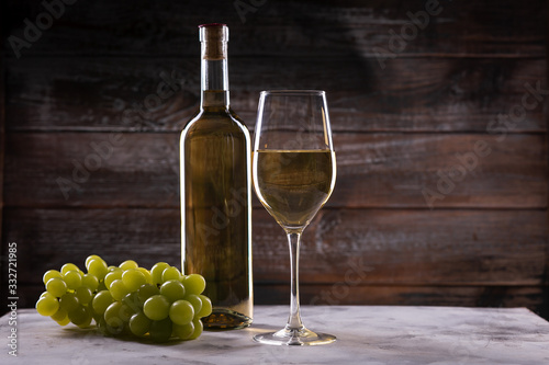 White full wine bottle and wineglass with grapes on a table on a wooden background
