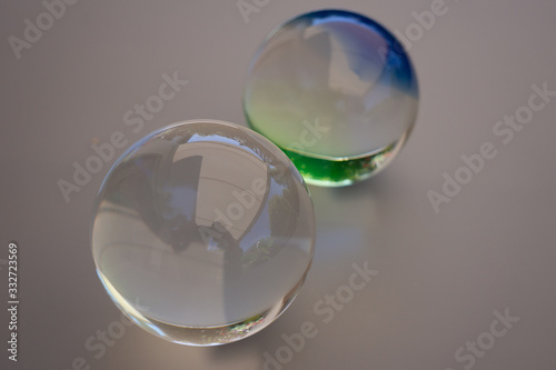 two individual glass balls against a gray background. One ball is crystal clear and the other shimmers green blue