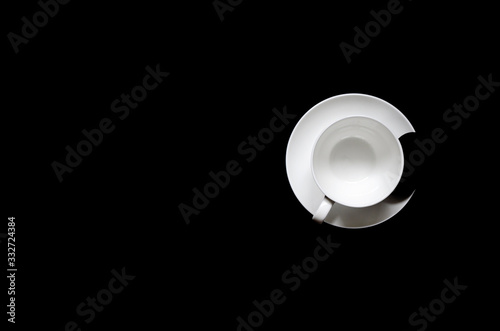 A white cup of coffee with black biscuits on a plate stands on a black background