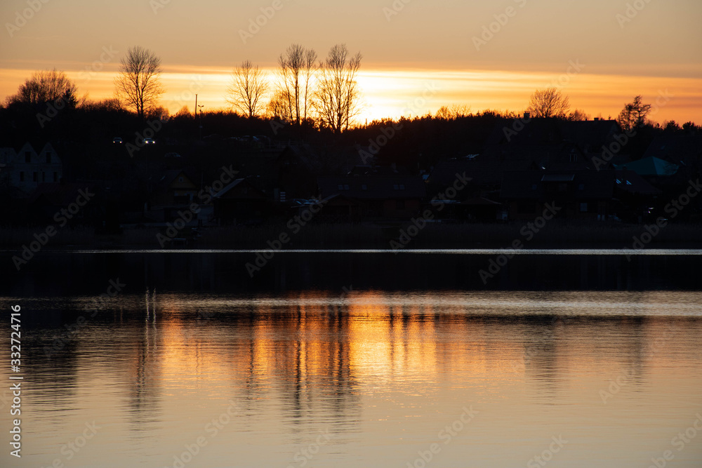 Beautiful sunset reflected on the water on a blue lake or river with silhouette of forest