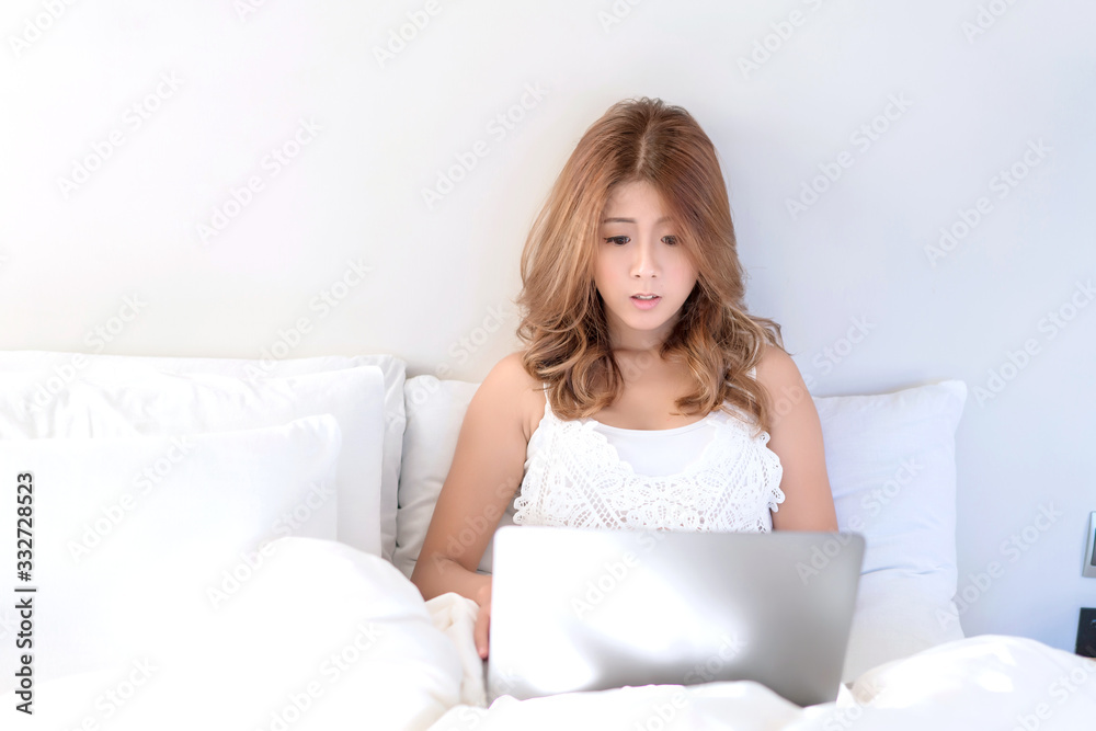 Young beautiful Asian female using laptop or notebook for working at home or shopping online while laying on bed in her bedroom. Communication Technology, marketing online, social media concept. Young beautiful Asian female using laptop or notebook for working at home or shopping online while laying on bed in her bedroom. Communication Technology, marketing online, social media concept.