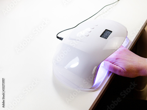 Female hand with red nails in a lamp for manicure. Lamp for nails Gel dryer Nail polish.