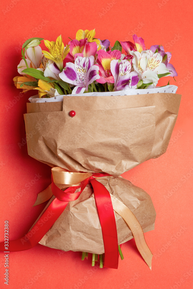 Fototapeta premium Aesthetic bouquet with multicolor alstroemeria flowers in craft paper with red pin decoration on red background. Woman international day or romantic date concept 