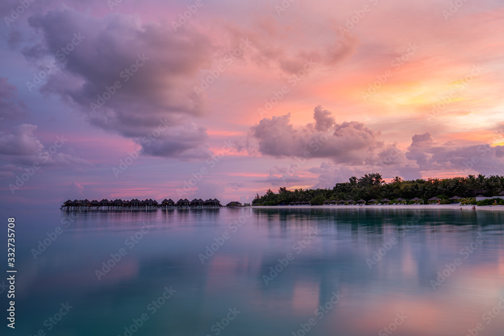 Amazing sunset landscape. Picturesque summer sunset in Maldives. Luxury resort bungalows seascape with soft led lights under colorful sky. Dream sunset over tropical sea, fantastic nature scenery