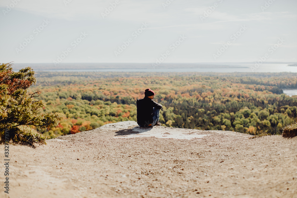 Φωτογραφία Homme assis au bord d'une falaise et contemplant la forêt