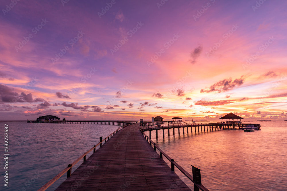 Sunset on Maldives island, luxury water bungalows villas resort and wooden pier. Beautiful sky and clouds and beach with seascape for summer vacation holiday and travel concept