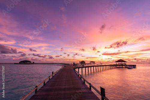 Sunset on Maldives island  luxury water bungalows villas resort and wooden pier. Beautiful sky and clouds and beach with seascape for summer vacation holiday and travel concept