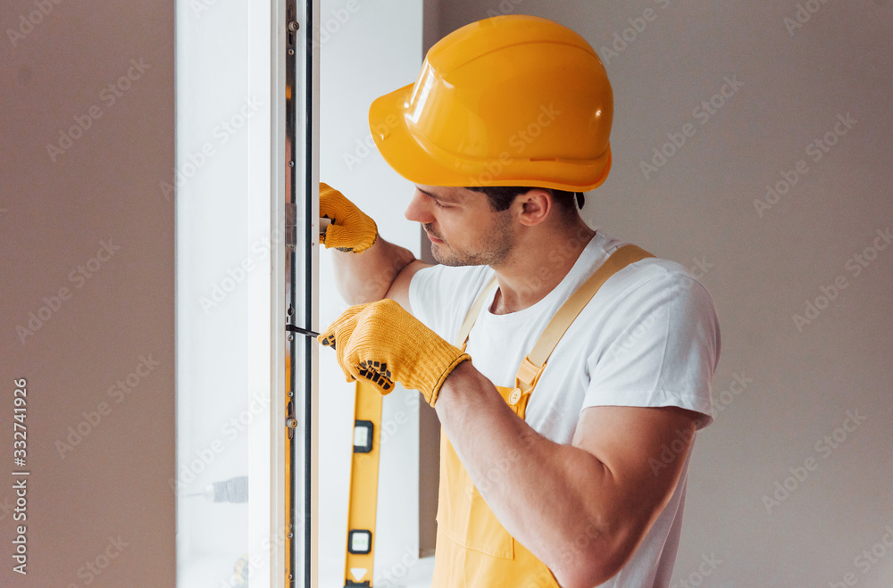 Handyman in yellow uniform installs new window. House renovation conception Handyman in yellow uniform installs new window. House renovation conception