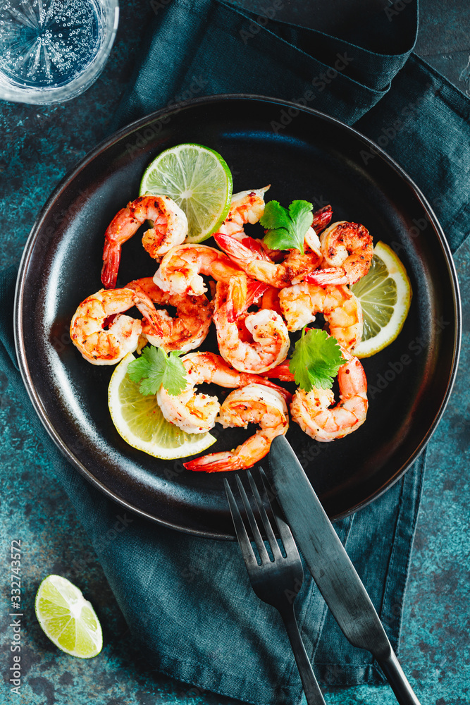 Fried tiger shrimp with lime, lemon and spices on a black plate. Healthy dinner or lunch concept.