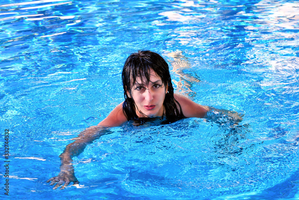 A beautiful girl is swimming in the swimming pool with blue water.
