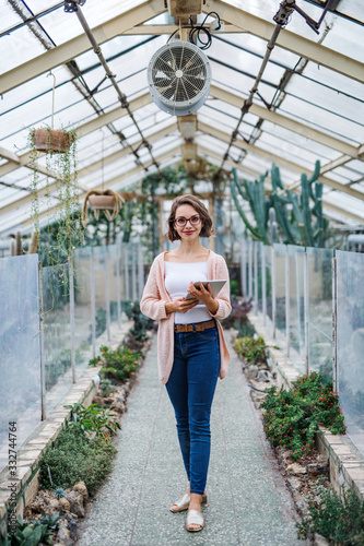 Woman researcher standing in greenhouse, using tablet.