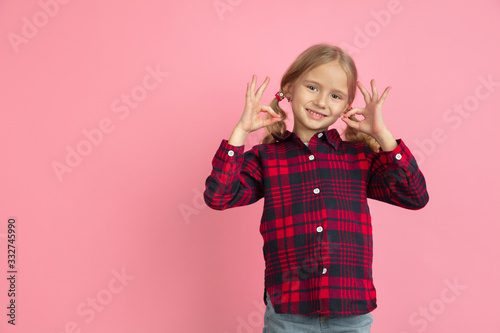 Showing nice gesture. Caucasian little girl's portrait on pink studio background. Beautiful female model with blonde hair. Concept of human emotions, facial expression, sales, ad, youth, childhood.