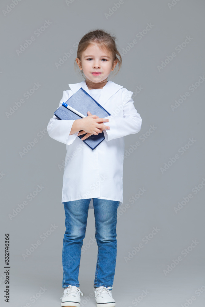 Adorable child girl uniformed as doctor is holding medical record isolated on grey background Adorable child girl uniformed as doctor is holding medical record isolated on grey background