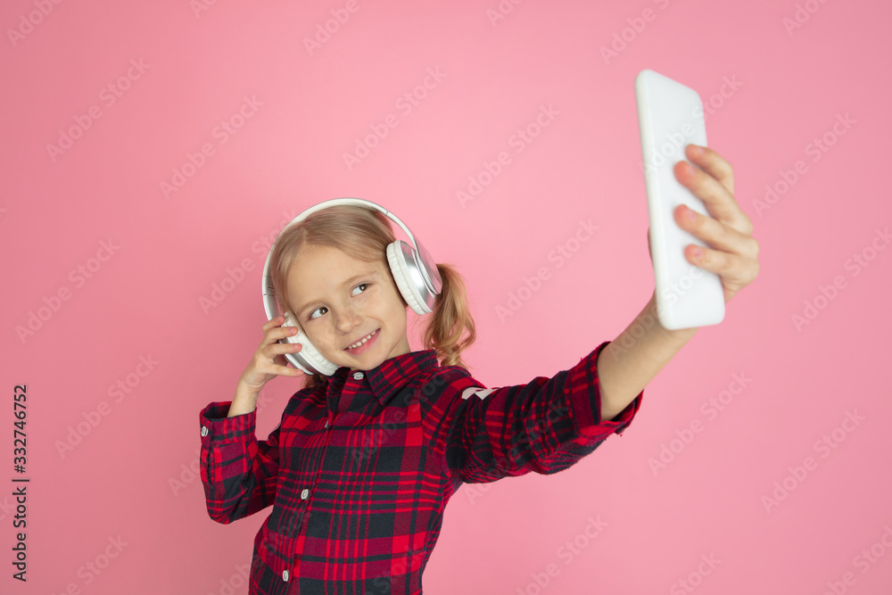 Taking selfie, vlog. Caucasian little girl's portrait on pink studio background. Beautiful female model with blonde hair. Concept of human emotions, facial expression, sales, ad, youth, childhood. Taking selfie, vlog. Caucasian little girl's portrait on pink studio background. Beautiful female model with blonde hair. Concept of human emotions, facial expression, sales, ad, youth, childhood.