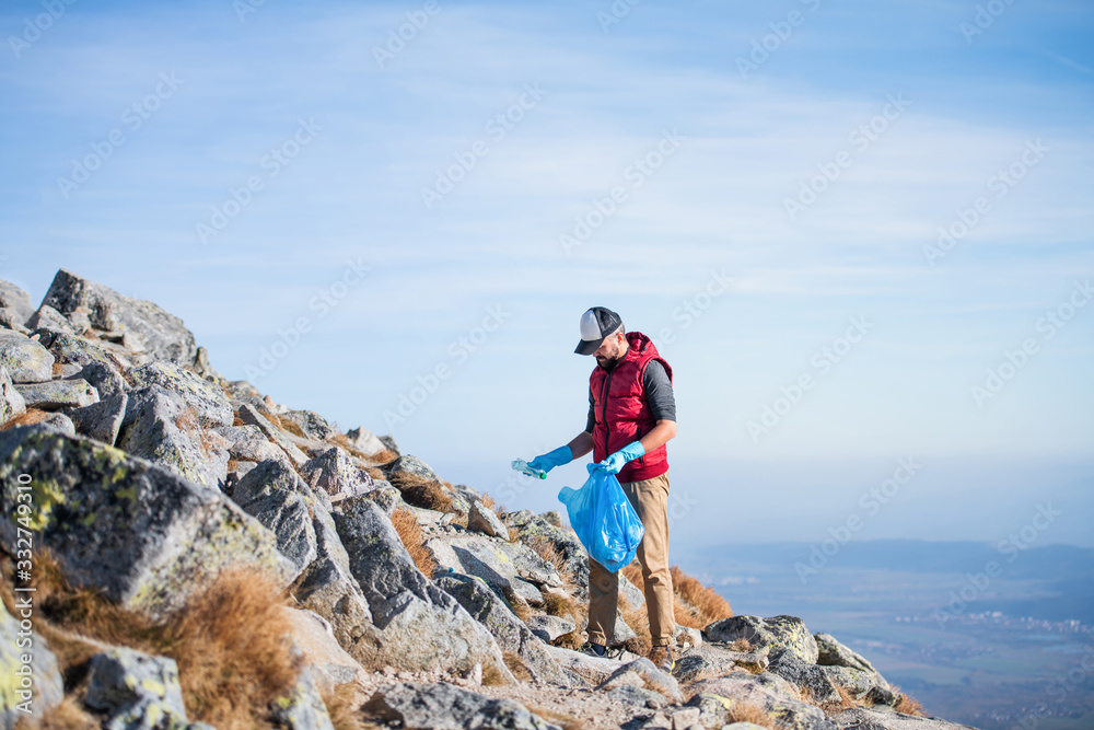 Man hiker picking up litter in nature in mountains, plogging concept.