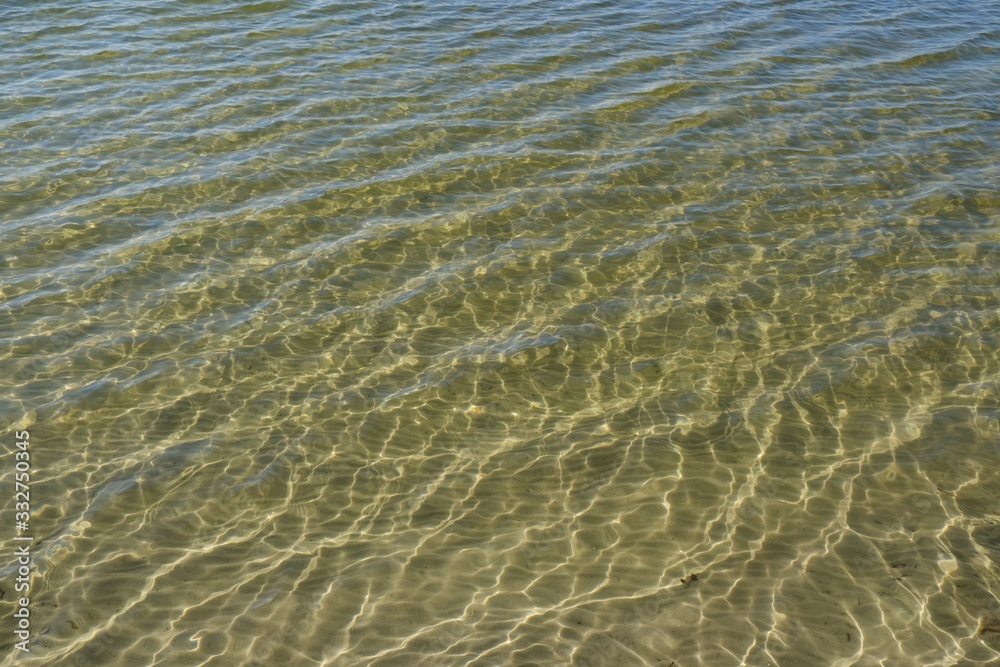 Transparent water in the lake - visible bottom with white sand and light reflections