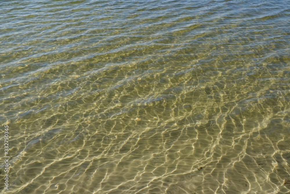 Transparent water in the lake - visible bottom with white sand and light reflections Transparent water in the lake - visible bottom with white sand and light reflections