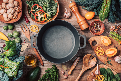 Various organic vegetables ingredients and empty iron cooking pot, wooden bowls, spoons on wooden background. Top view, copy space. Organic vegetables ingredients for vegan cooking. Clean eating food © jchizhe
