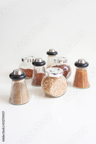 Various spices in glass jars. Ground black and red pepper, cardamom, ground cinnamon, parsley root, spice mix