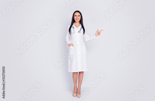 Full body photo of cheery professional practitioner lady advising patient novelty direct finger empty space wear long white lab coat stethoscope high-heels isolated grey color background
