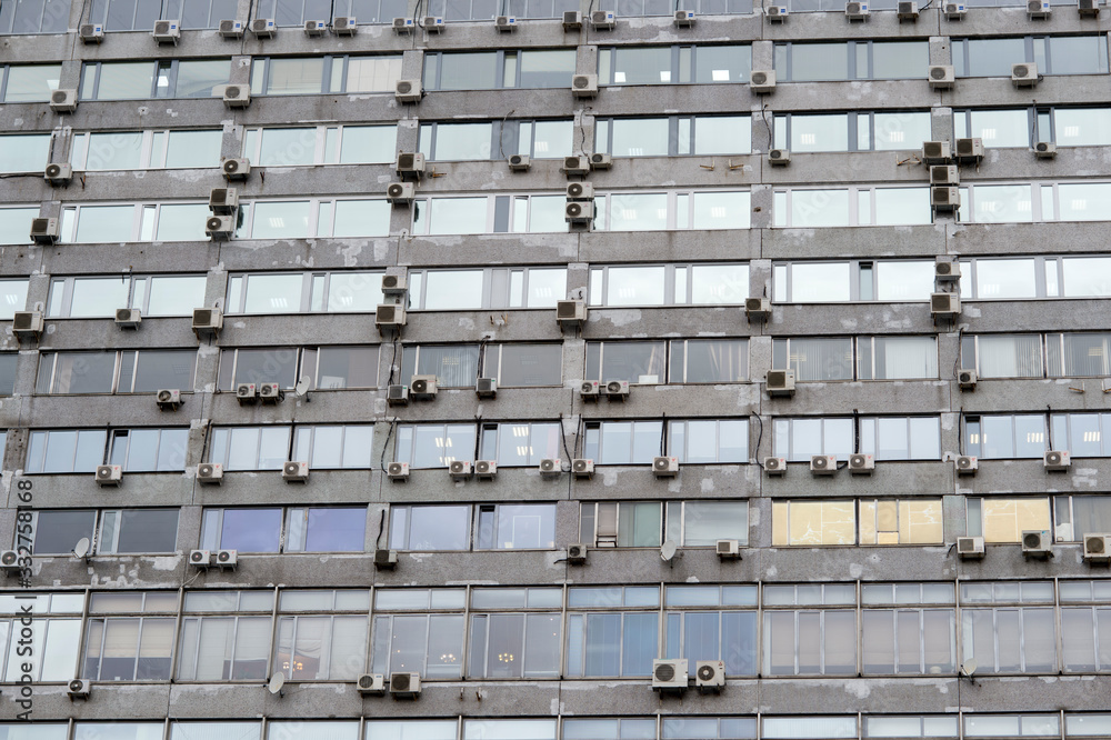 The wall of a large gray office building is studded with air conditioners of various brands, Russia, Moscow, March, 2020