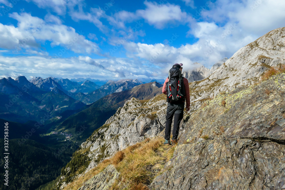 Man reaching the top of Monte Coglians, Hohe Warte on Austrian-Italian Alpine border. Very steep and narrow pathway that he walks on. He is enjoying the landscape. Goal visualization. Stunning view